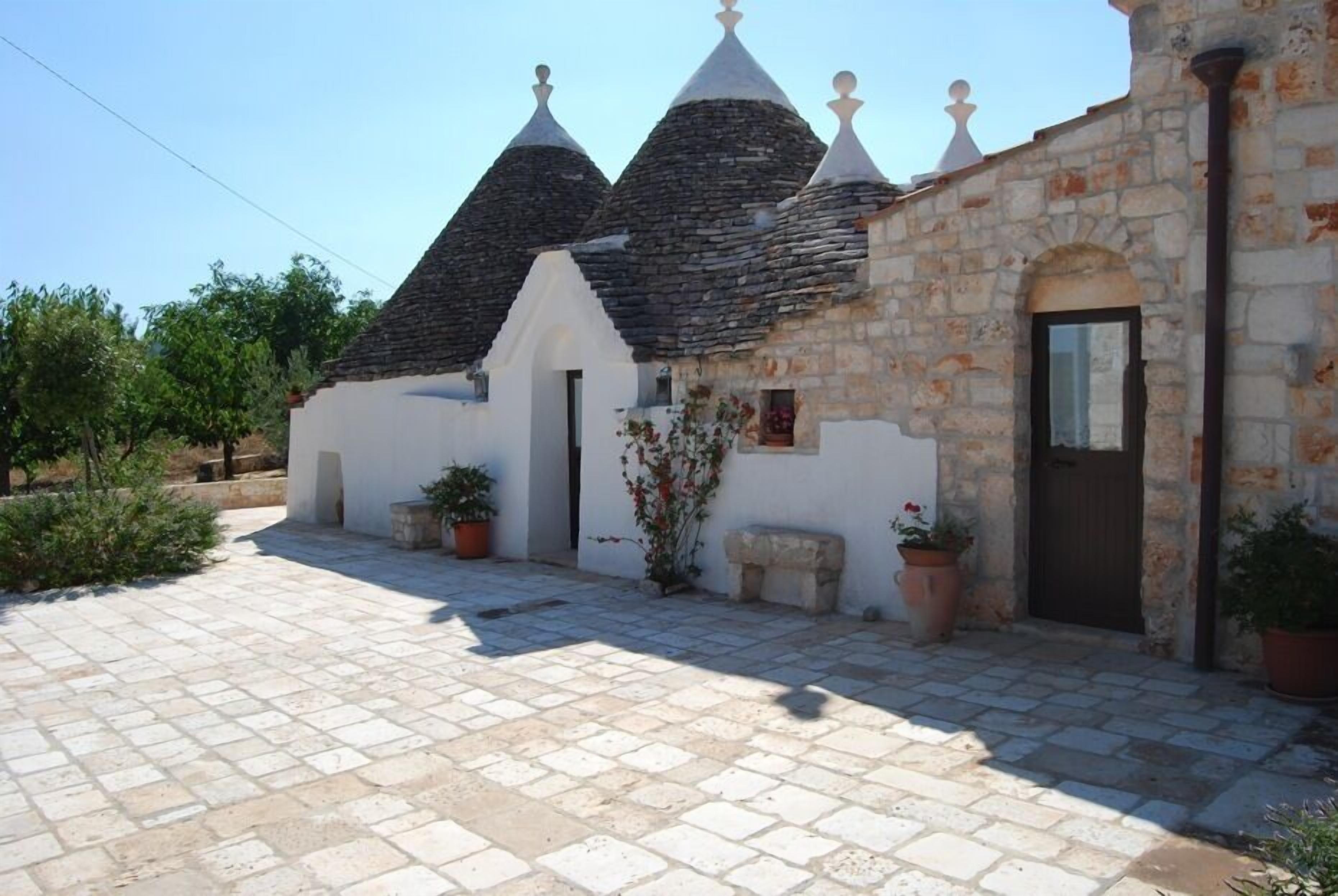 A stone building with a tiled courtyard, a door, and potted plants.