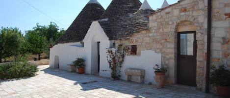 A stone building with a tiled courtyard, a door, and potted plants.