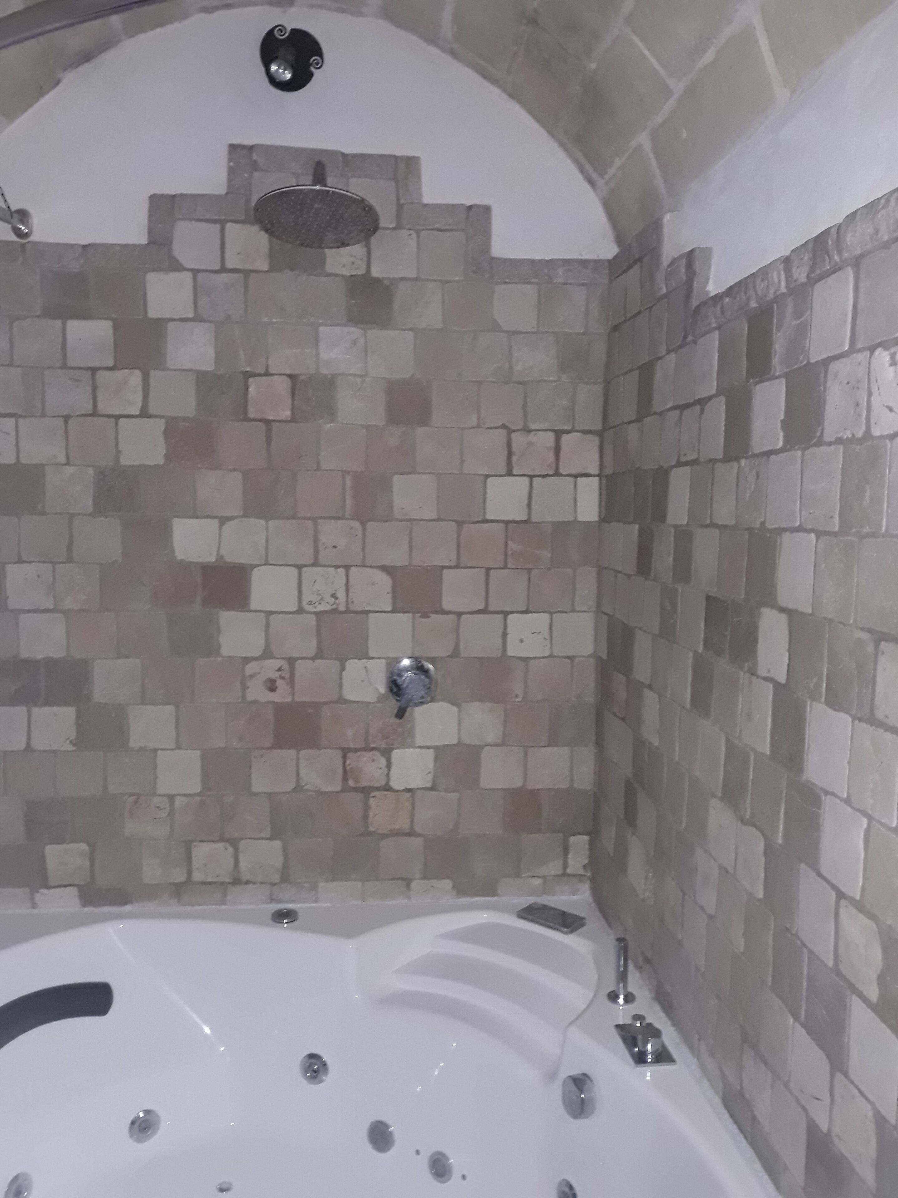 A bathroom with a tiled shower wall, a bathtub, and a showerhead.