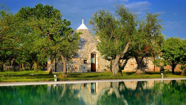 A stone building with a dome roof, surrounded by trees and a reflecting pool.