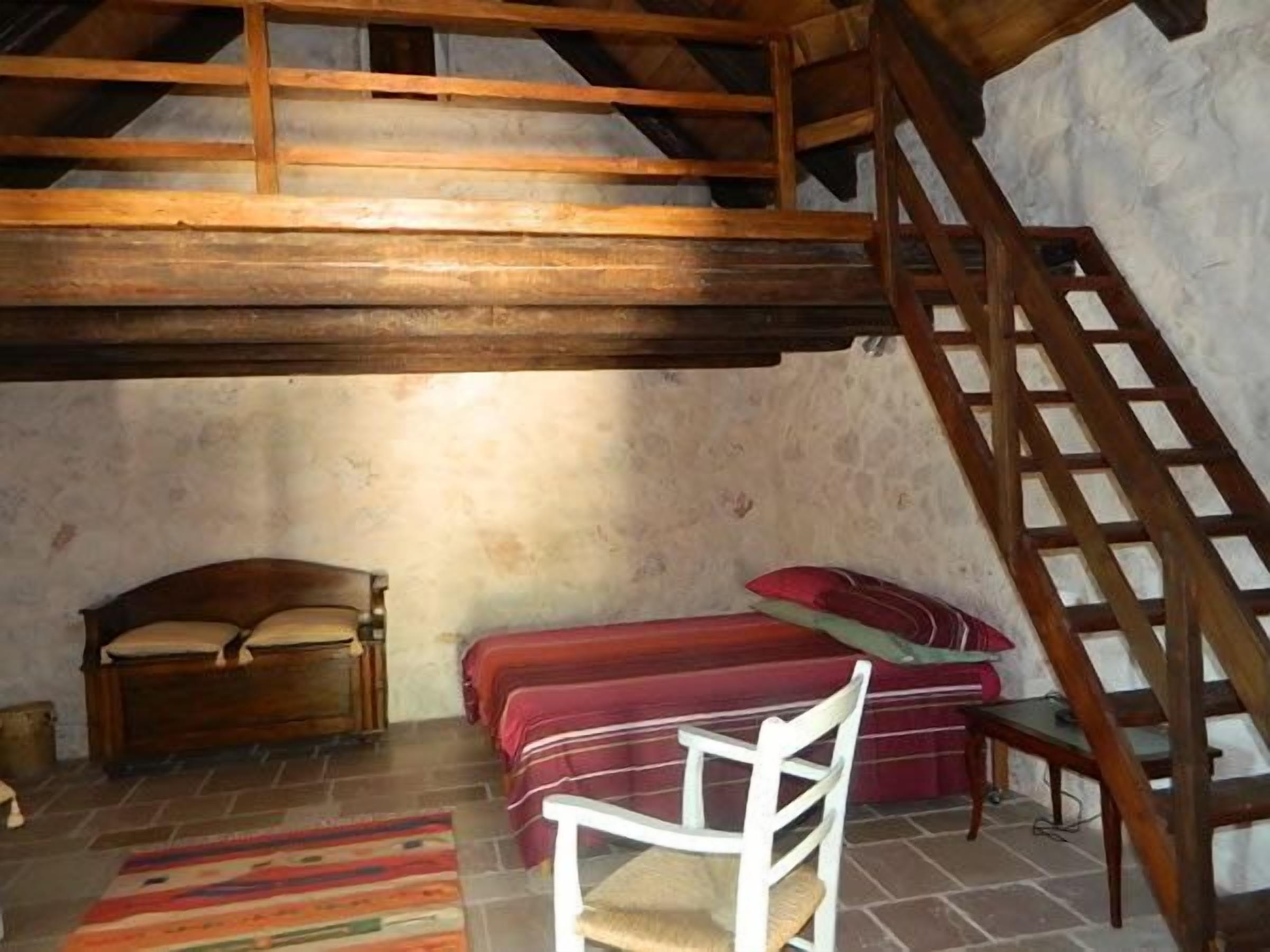 A rustic room with a loft bed, a wooden chair, and a staircase.