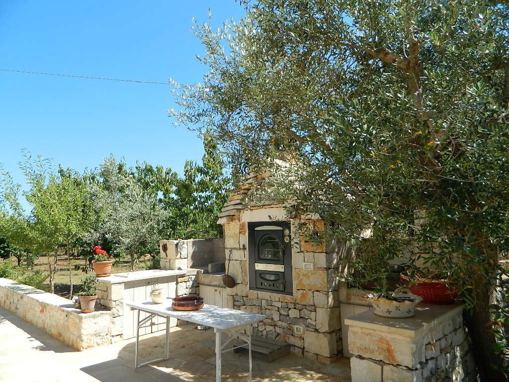 Angolo cucina esterno con forno a pietra, un tavolo e piante in vaso.