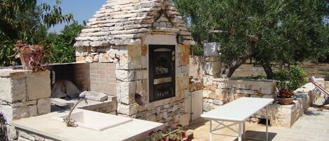 An outdoor stone-built barbecue area with a built-in oven, a sink, and a table.