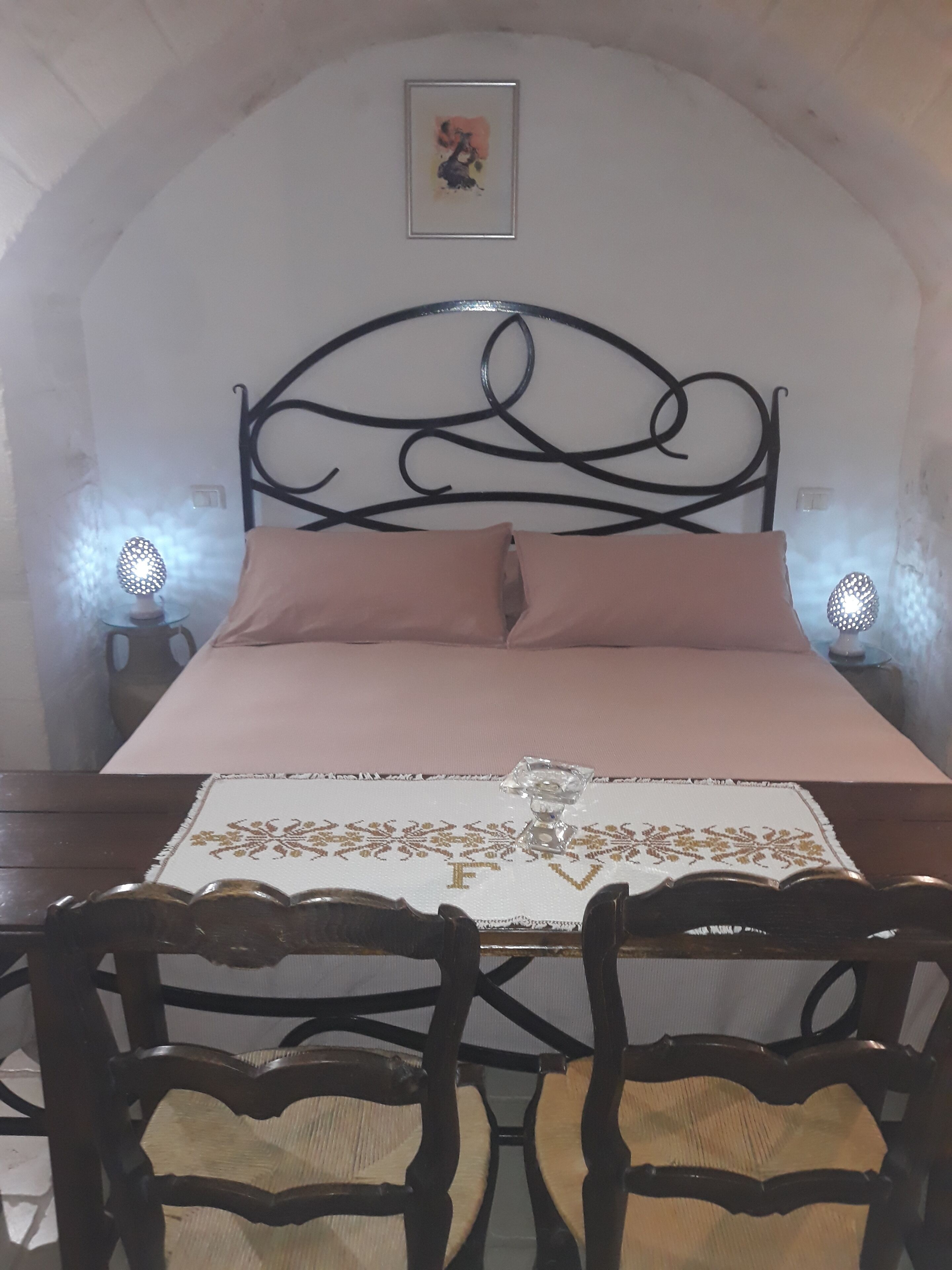 A bedroom with a bed, a headboard, bedside lamps, and a framed picture on the wall.