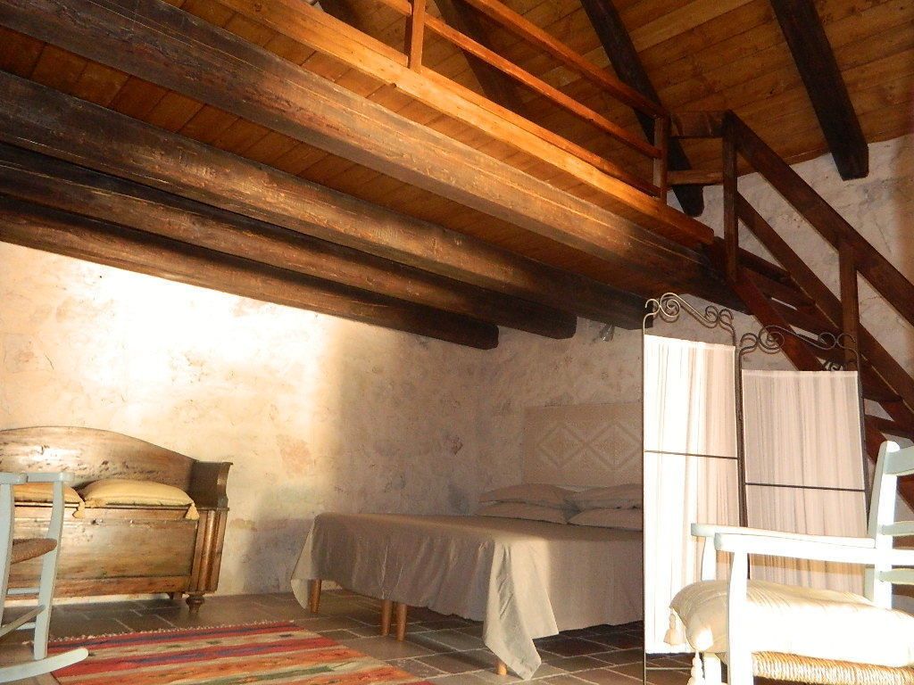 A rustic bedroom with exposed wooden beams, a single bed, a chair, and a small table.