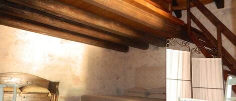 A rustic bedroom with exposed wooden beams, a single bed, a chair, and a small table.
