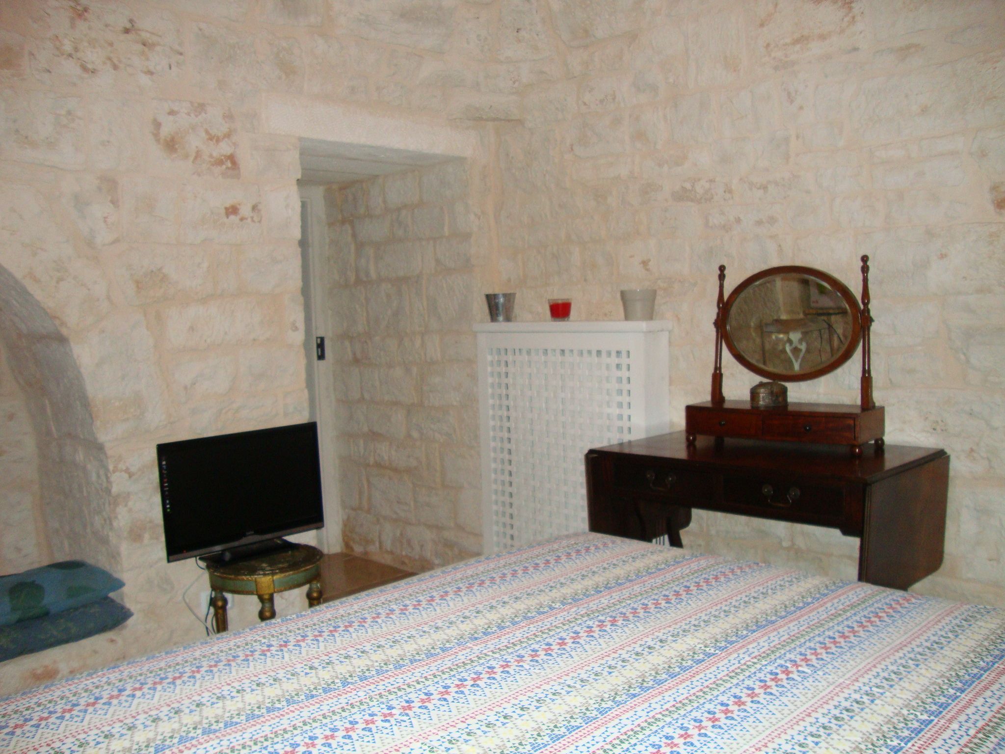 A bedroom with a bed, a dresser, a mirror, a television, and a stone wall.