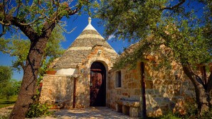 A stone building with a conical roof, surrounded by trees and grass.