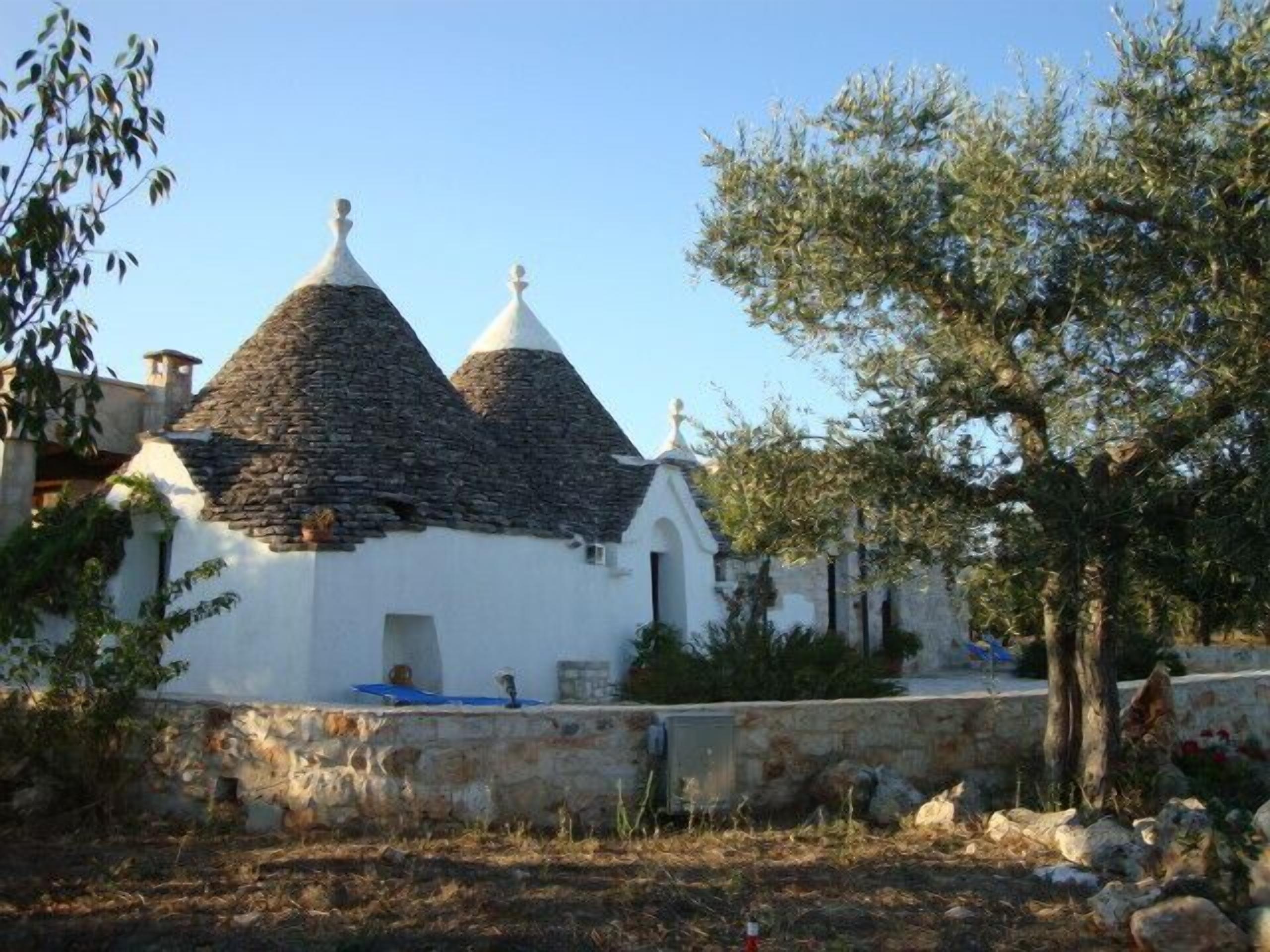 A traditional stone-roofed building with a white facade, surrounded by trees and a stone wall.
