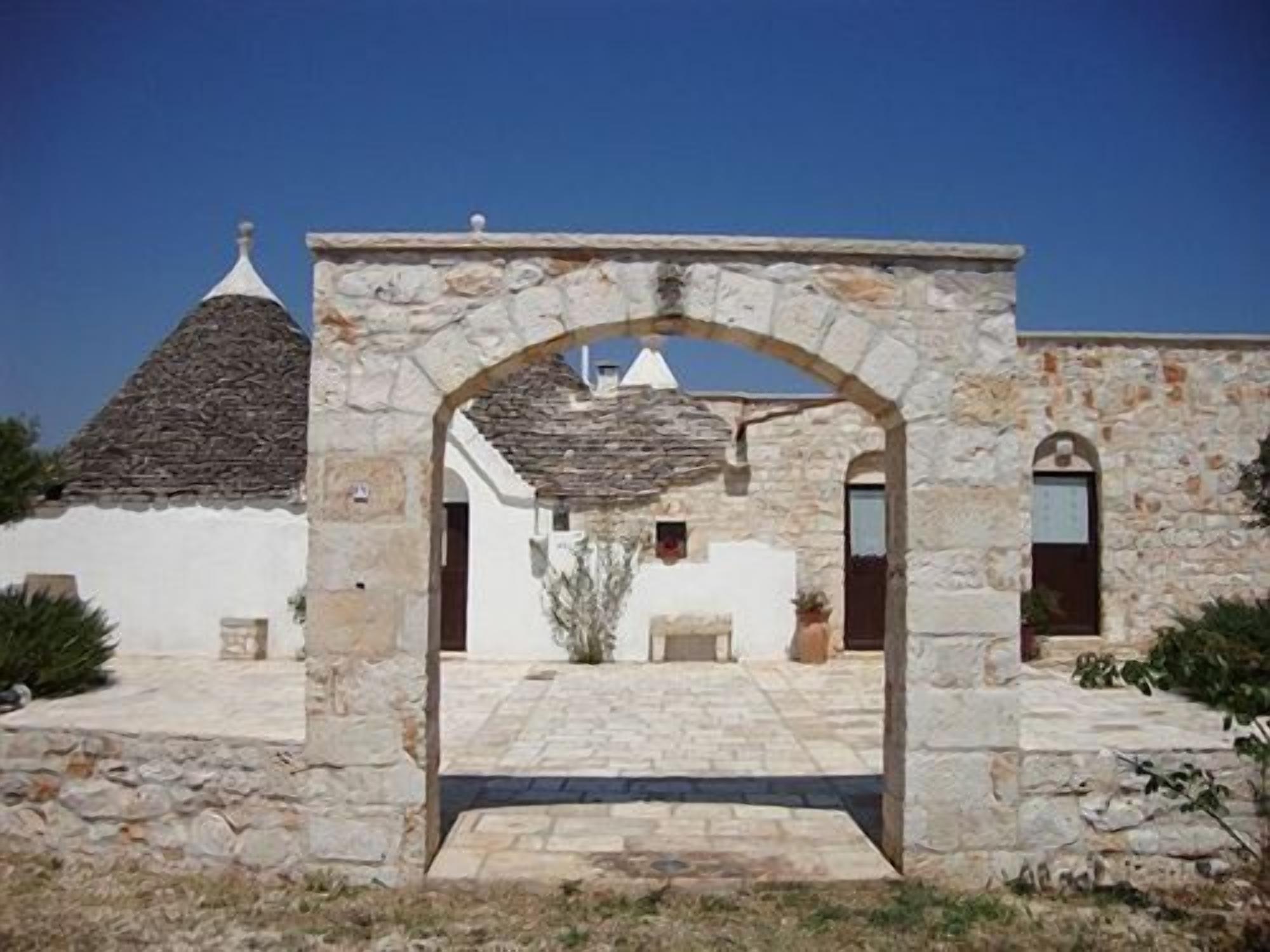 A stone archway leading to a courtyard with a tiled floor, surrounded by buildings with stone walls and tiled roofs.
