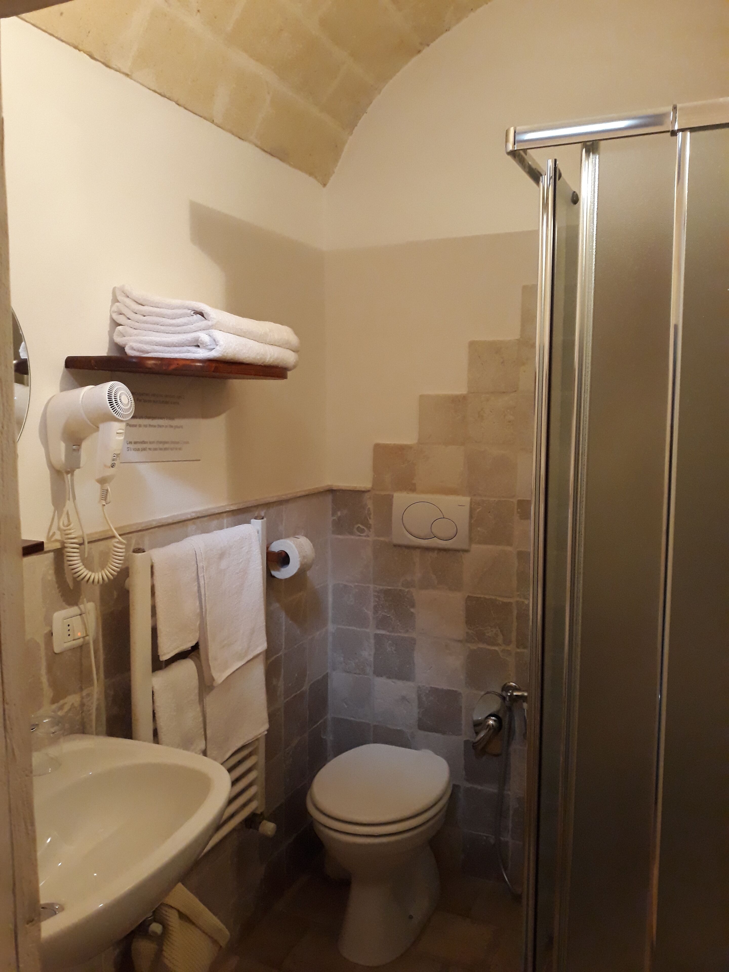 A bathroom with a sink, toilet, and a glass-enclosed shower. There is a towel rack with folded towels and a hairdryer on the wall.