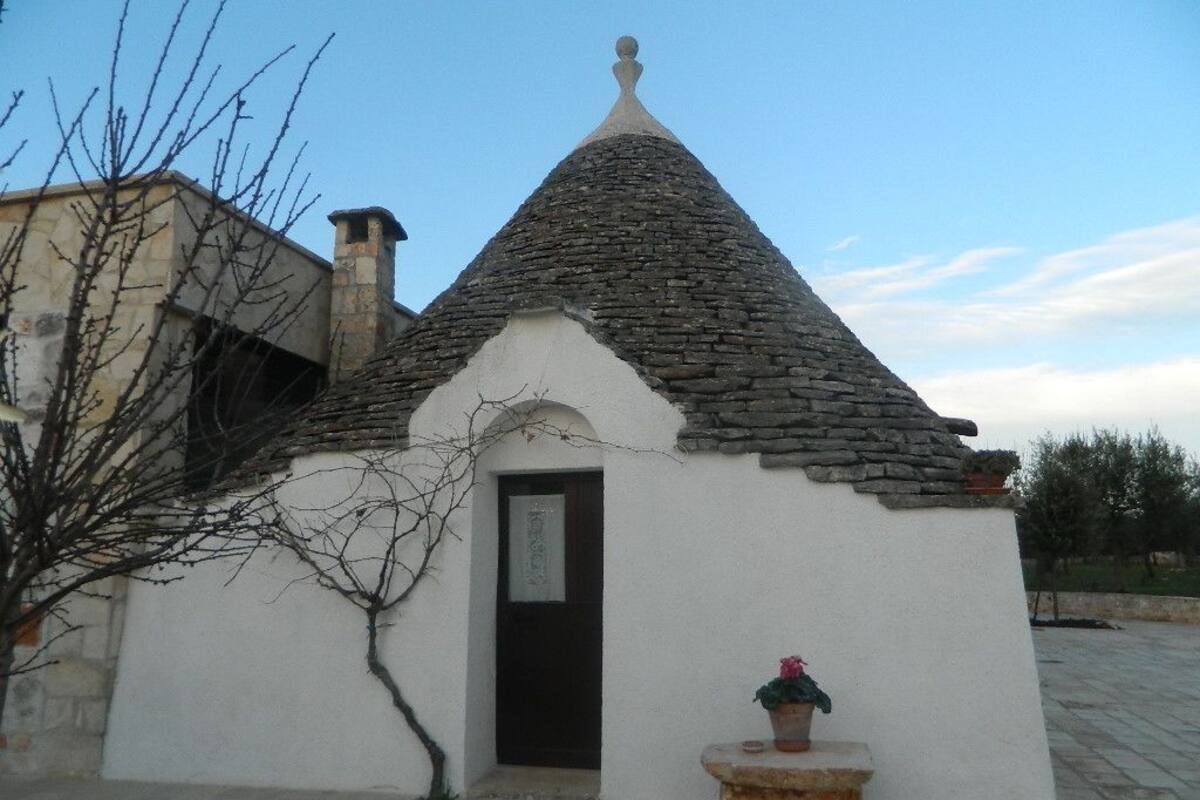Una pequeña construcción con techo cónico, una puerta y una planta en maceta.