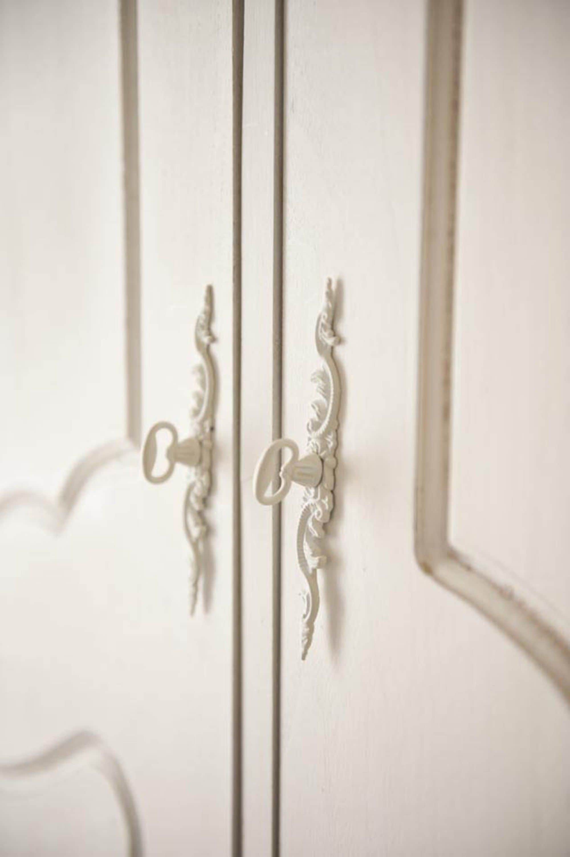 Une porte blanche ornée de poignées symétriques et travaillées.