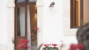 A white building with a large arched doorway, a small window, and a potted plant with red flowers. - Dimora Donna Lucrezia (Fasano)