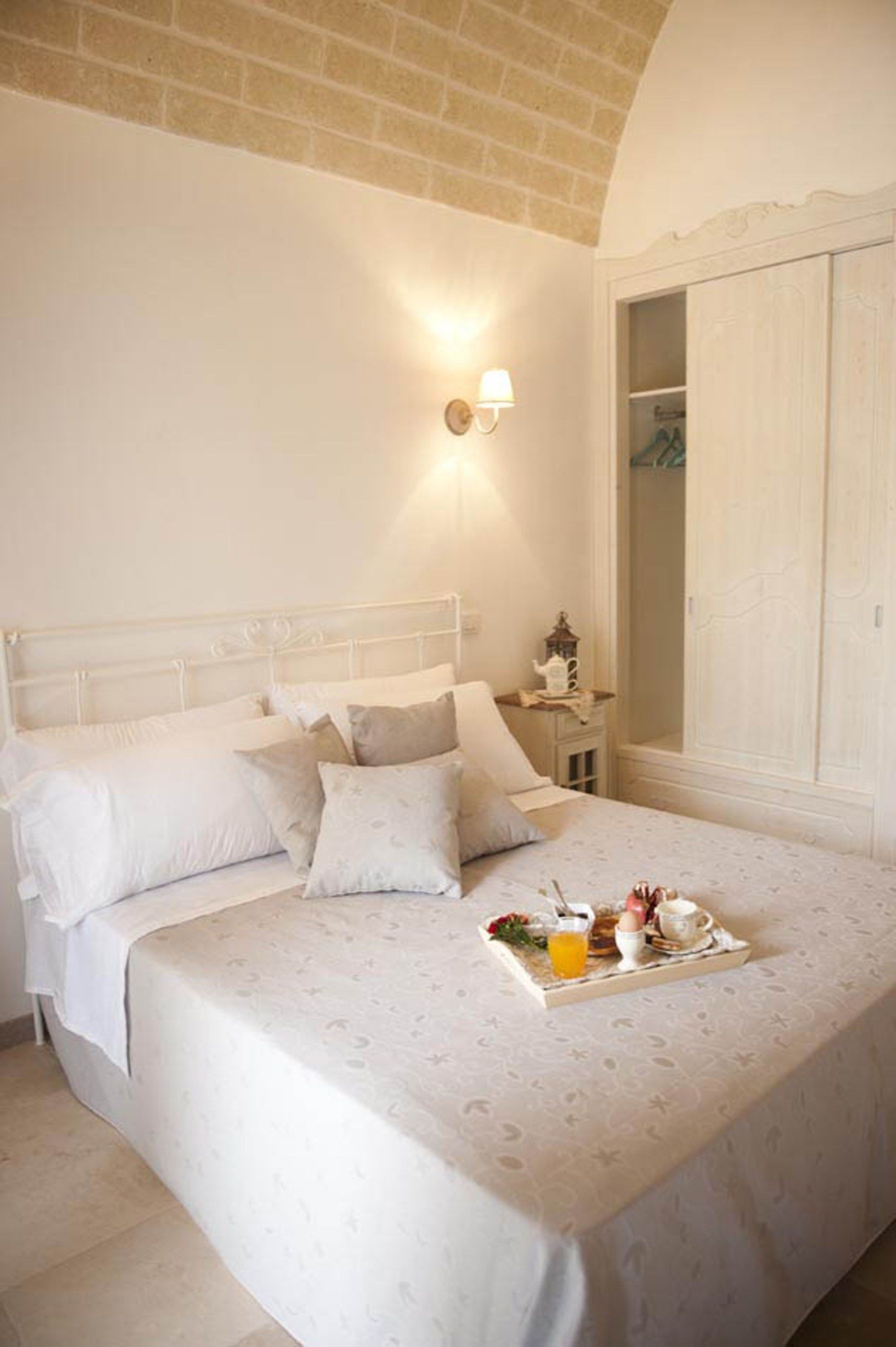 A bedroom with a large bed, a bedside table with a lamp, and a tray with breakfast items.