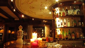 Zona de bar con una mesa redonda, velas y una variedad de botellas de licores.