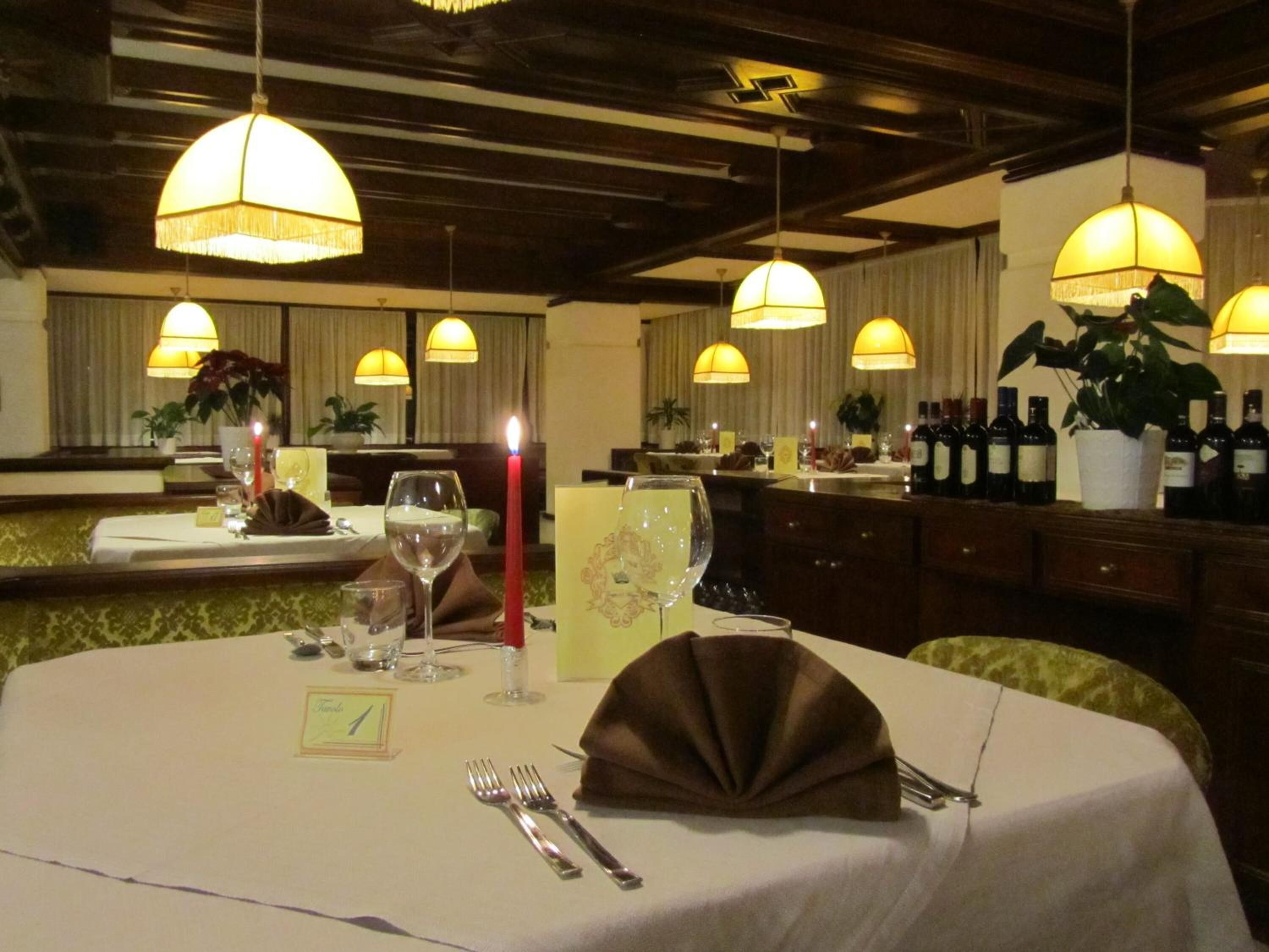 Uma área de refeições com mesas redondas, velas, copos de vinho e um bar com garrafas.