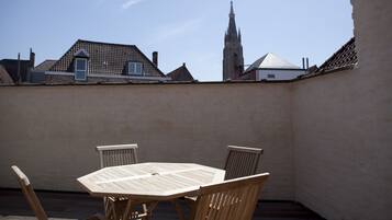 A rooftop patio with a round wooden table and four chairs, overlooking a cityscape with traditional buildings and a church spire.