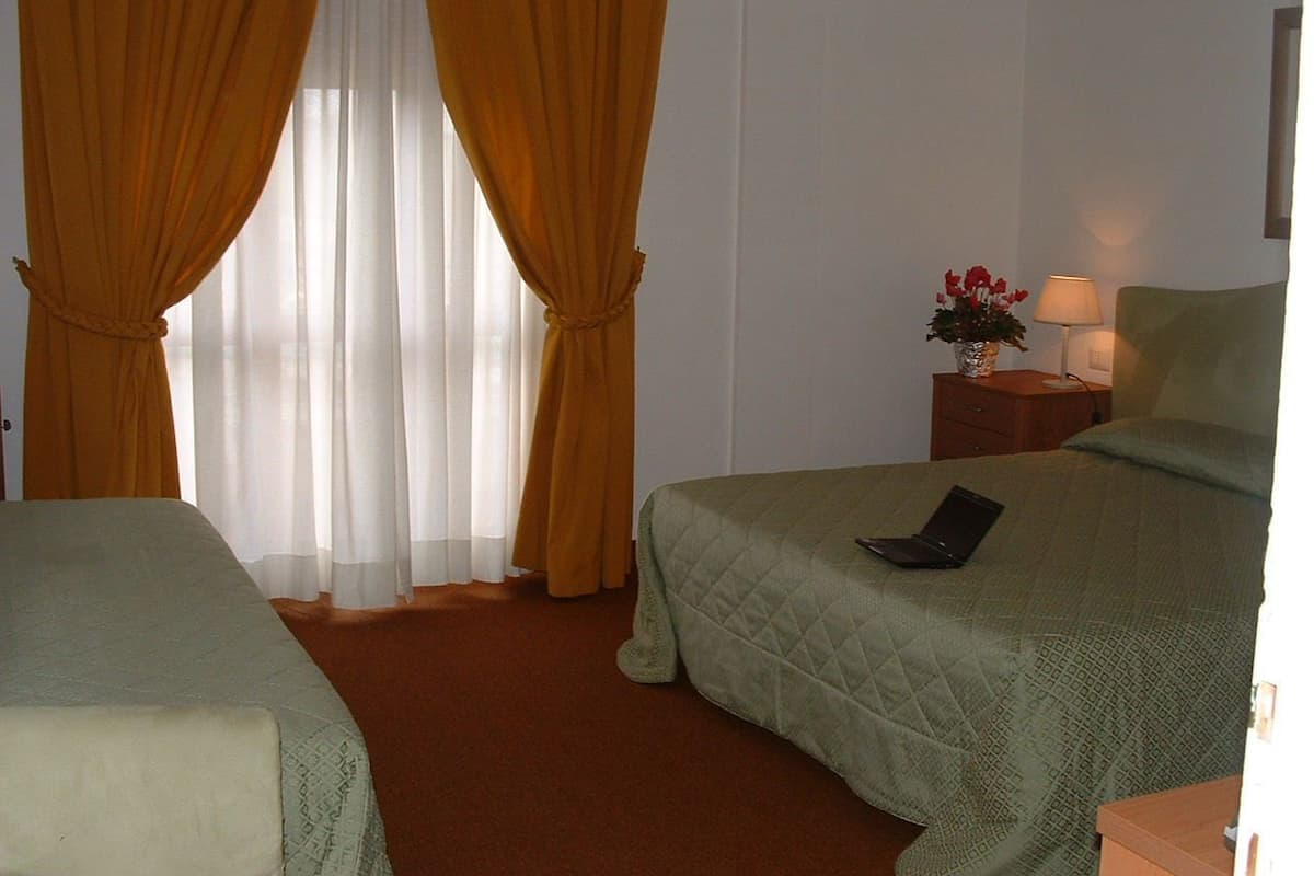 A hotel room with two beds, a nightstand with a lamp, and a window with curtains.