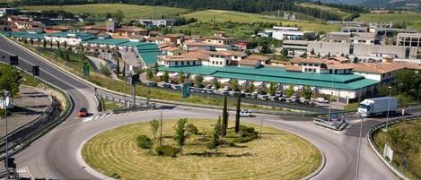 Una glorieta con un islote central cubierto de césped, rodeada de edificios con techos verdes y una combinación de locales comerciales y viviendas.