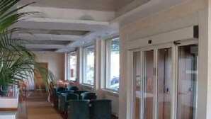 Eine Hotellobby mit einer langen Korridor, einer Sitzecke mit Stühlen, großen Fenstern und einer Pflanze.