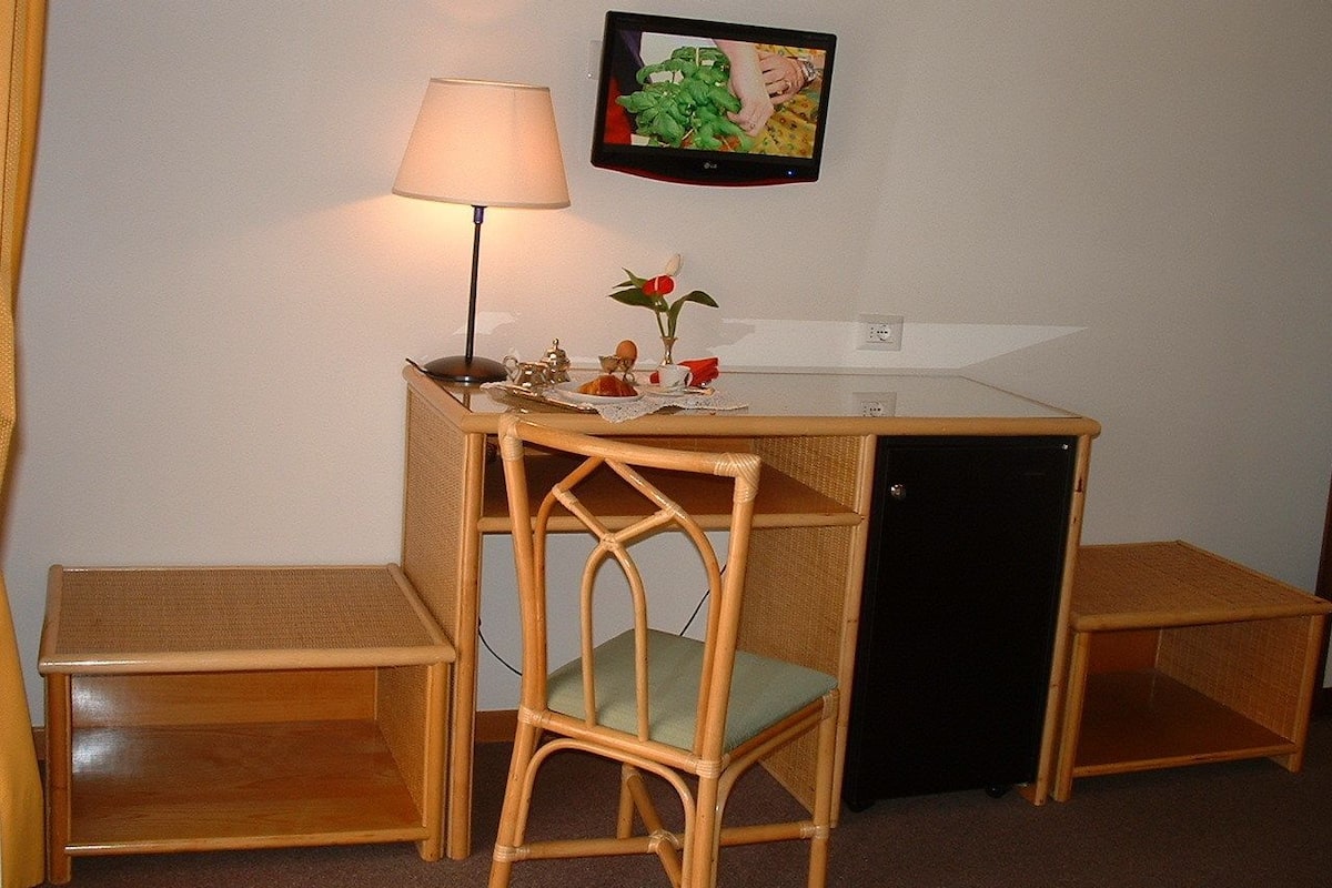 A small, compact room with a desk, a chair, a lamp, and a television mounted on the wall.