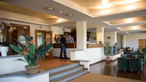 Eine Hotelhalle mit Empfangstresen, einer Treppe und einer grünen Sitzecke.