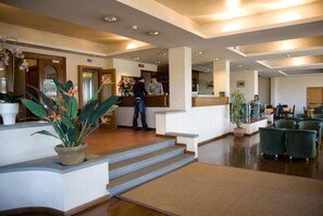 A hotel lobby with a reception desk, a staircase, and green seating area. - Hotel Barberino (Barberino di Mugello)