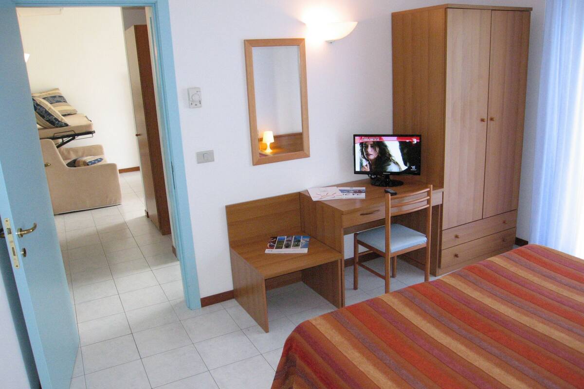 A hotel room with a bed, a desk, a chair, a television, a wardrobe, and a massage chair.