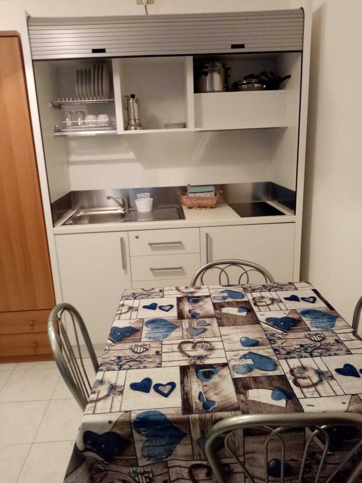 Eine kompakte Küche mit integriertem Spülbecken, einer kleinen Arbeitsfläche und einem Esstisch mit Tischdecke mit Herzmuster.