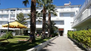 Un hotel con recepción, mesas al aire libre, palmeras y cielo despejado.