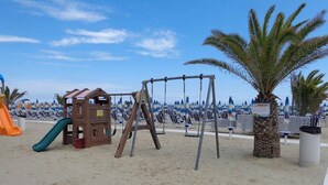 Un parque infantil en la playa con tobogán, columpios y una casita.