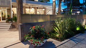 A modern hotel entrance with a large flower bed, a well-lit pathway, and a view of the building's interior. - Hotel Belvedere (Cervia)