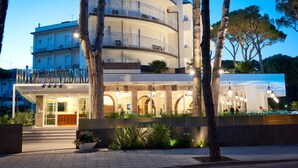 A multi-story hotel with a curved facade, outdoor seating area, and a well-lit entrance. - Hotel Belvedere (Cervia)