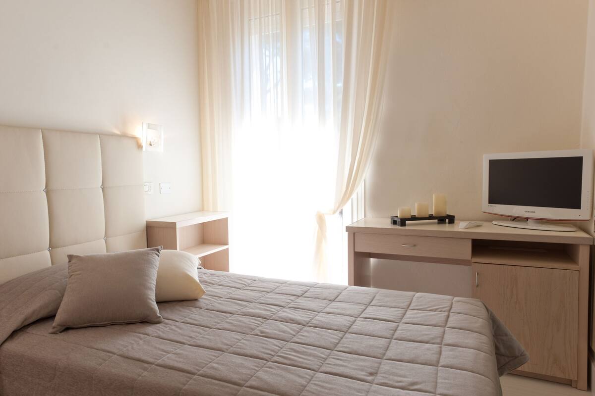 A bedroom with a bed, bedside table, desk, and a television.