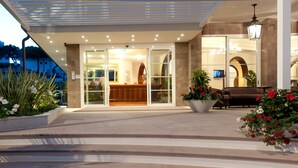 A hotel entrance with a reception desk, a staircase leading up, and potted plants. - Hotel Belvedere (Cervia)