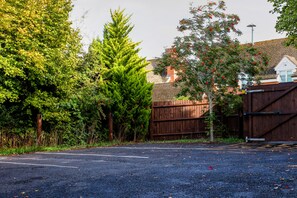 A parking area with a wooden fence, trees, and a building with a tiled roof. - The George Hotel (Newent)