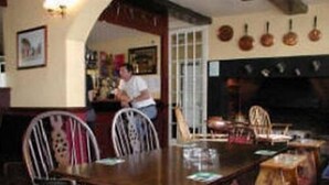 A dining area with a wooden table and chairs, a fireplace, and a bar area in the background.