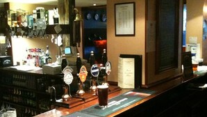 A bar area with multiple beer taps, a glass of beer, and a menu board.