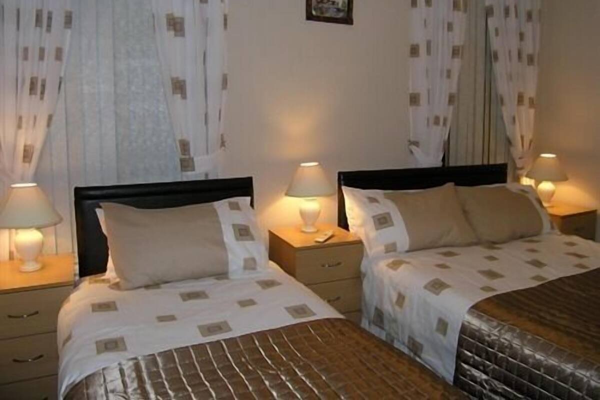 A hotel room with two beds, each with a nightstand, a lamp, and a small table.