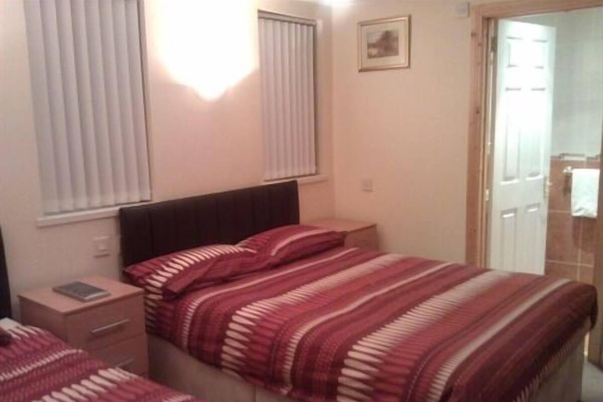 A bedroom with two beds, a nightstand, a bedside table, and a window with blinds.