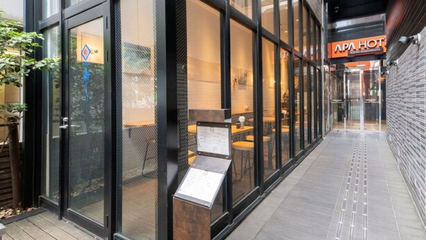 Un edificio moderno con grandes ventanales, una terraza de madera y un letrero que dice 'APA HOTEL TOKYO KUDANSHITA'.