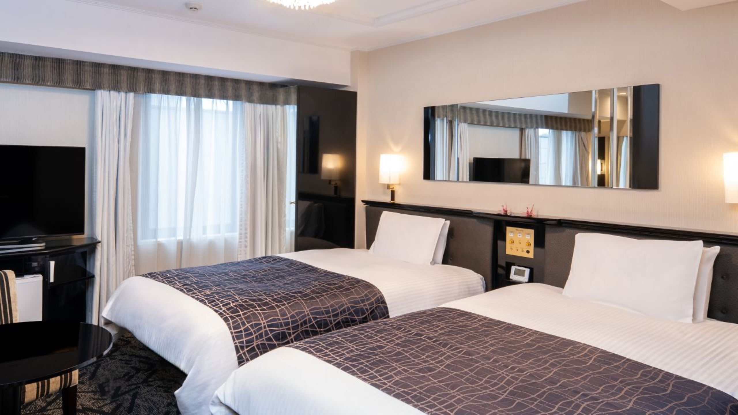 Quarto de hotel com duas camas, uma escrivaninha, televisão e um espelho grande.