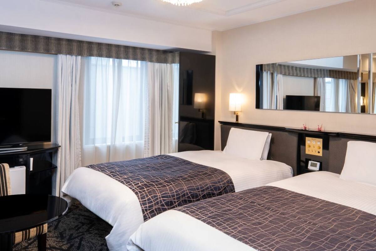 A hotel room with two beds, a desk, a TV, and a large mirror.