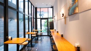 Interior moderno de una cafetería con mesas y sillas de madera, ventanas amplias y vista a la calle.