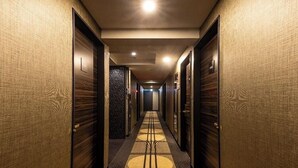 Un pasillo de hotel con piso estampado, puertas de madera y una lámpara central.