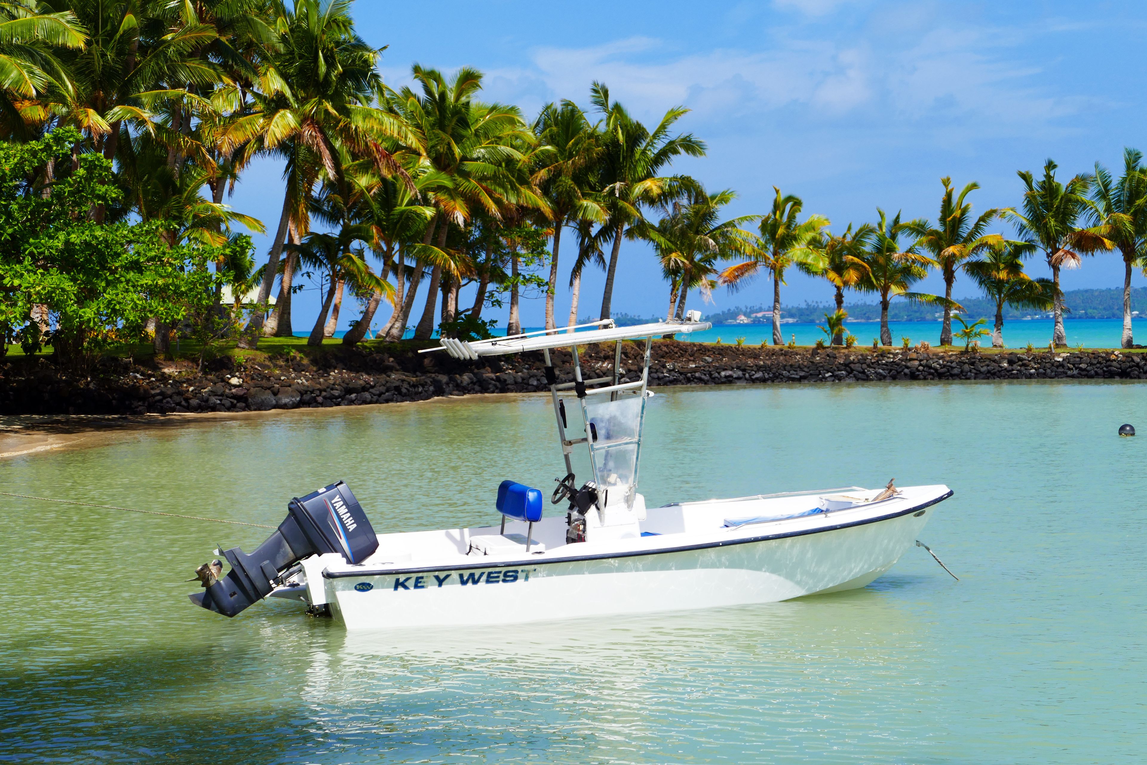 Un barco llamado "KEY WEST" anclado cerca de una playa con palmeras y agua azul cristalina.