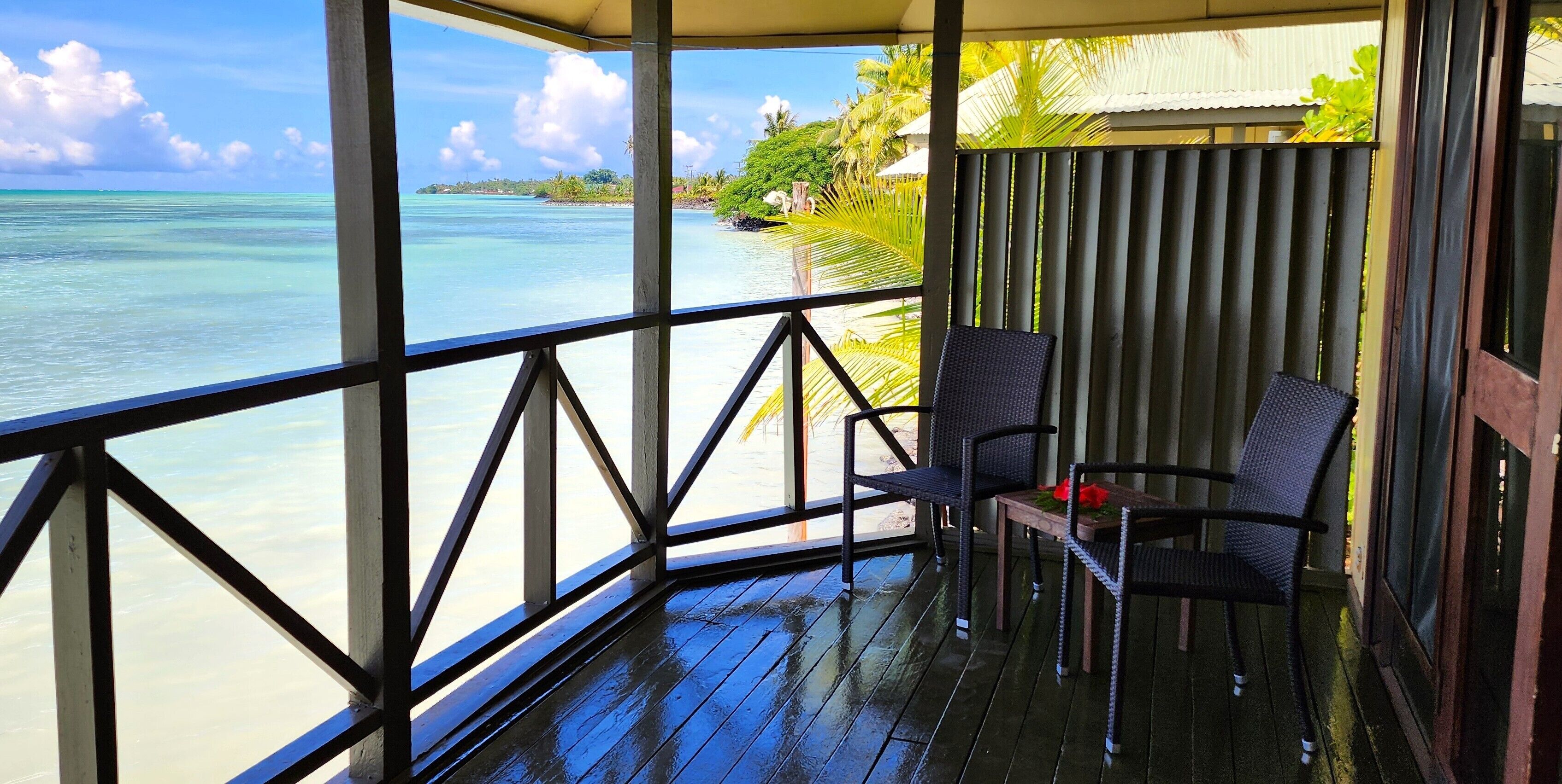 A covered outdoor area with a wooden deck, two chairs, and a view of the ocean and beach.