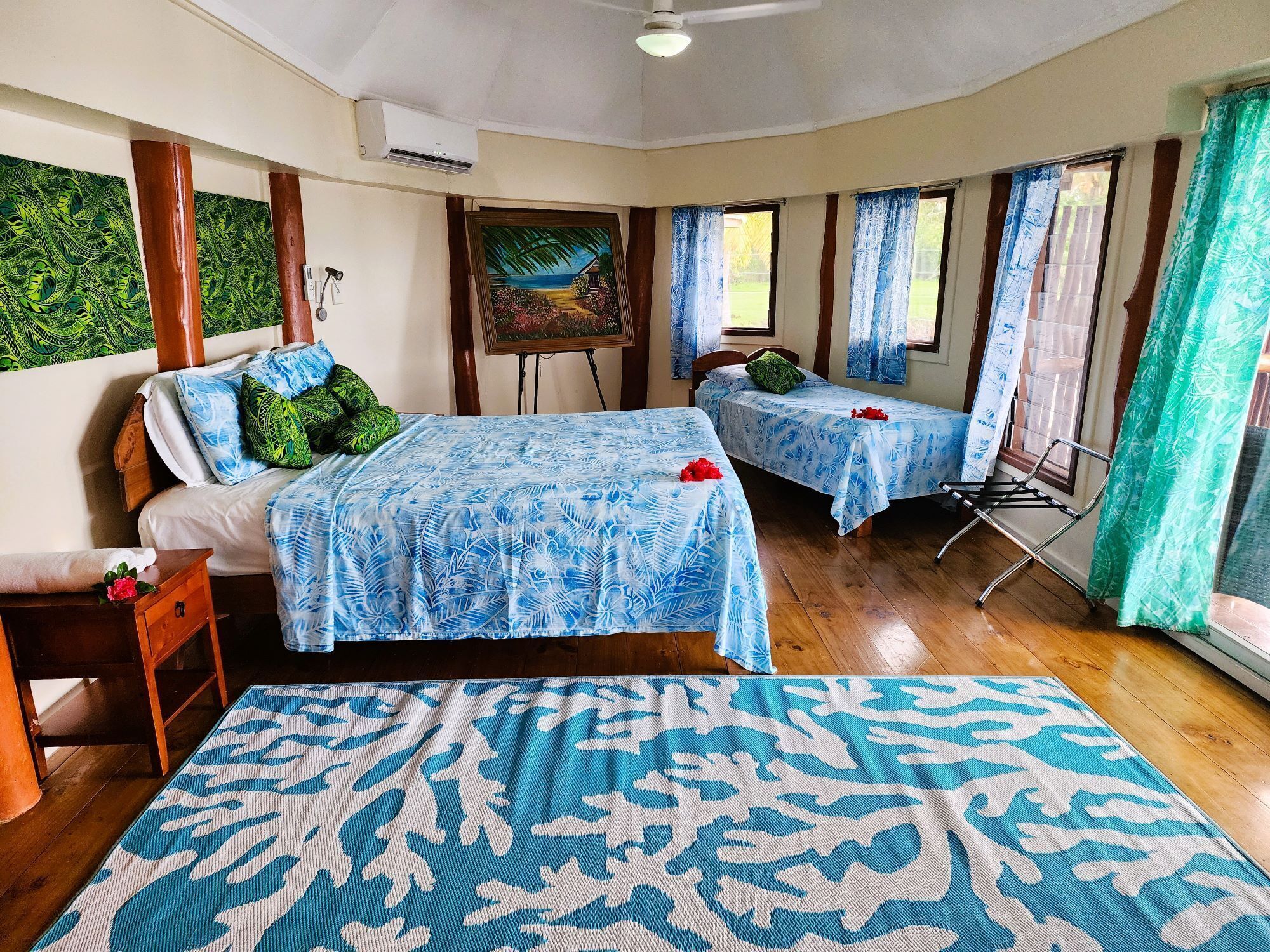 Une chambre avec deux lits, un tableau au mur et une fenêtre avec des rideaux.