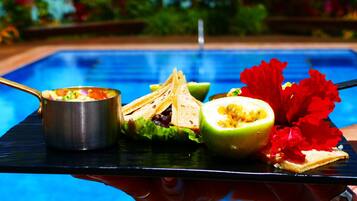 A dining table with a salad, tortilla chips, and a halved fruit next to a pool.